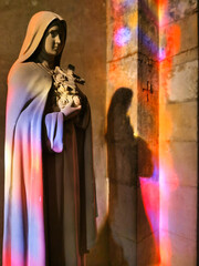 Saint therese of lisieux statue, with magnificent stained glass reflections, in a french catholic church.