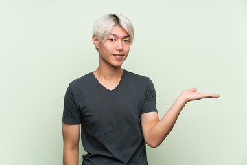 Young asian man over isolated green background holding copyspace imaginary on the palm to insert an ad
