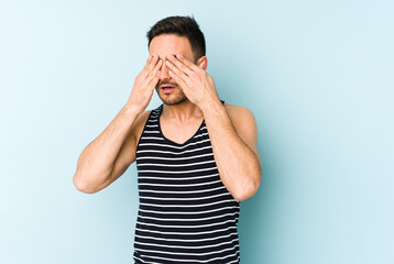 Young caucasian man isolated on blue background afraid covering eyes with hands.