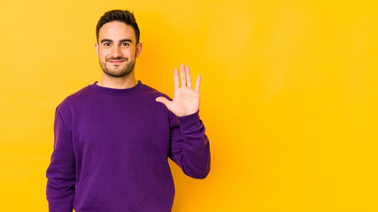 Naklejka premium Young caucasian man isolated on yellow bakground smiling cheerful showing number five with fingers.