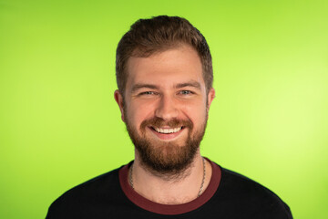 Fototapeta premium Funny bearded man broadly smiles on green background. Studio portrait of young happy Man looking at camera. Positive Male Caucasian model on chromakey background. High quality photo.