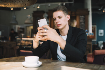 Young man messaging on phone in cafe
