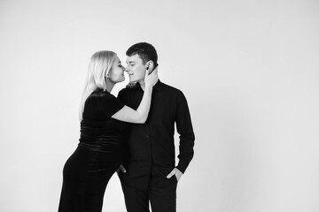 Pregnant woman and her husband smiling in black clothes on a white background. Black and white picture. Beautiful married couple. Copy, empty space for text