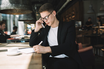 Young boss answering phone call while having daily business in cafe during break