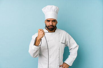 Young latin chef man isolated showing fist to camera, aggressive facial expression.