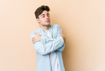 Young caucasian man isolated on beige background hugs, smiling carefree and happy.