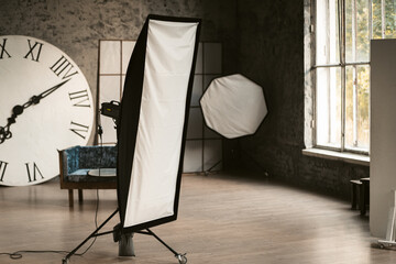 Studio light in a decorated photo studio. There's a big watch and a sofa in the background. Grey interior. High quality photo.