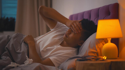 Sick Asain Guy having headache Lying In Bed At Home.