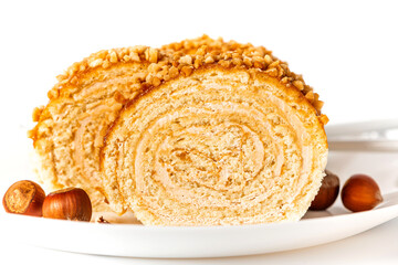 Homemade sweet roll cake with nuts and cream filling in a plate on a white background close-up. Free space for text. Sweet food, homemade cakes. Copy space.