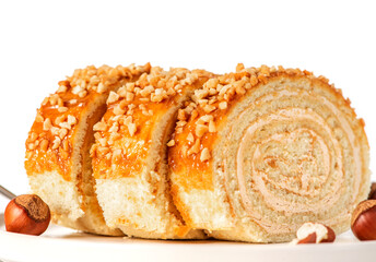 Homemade sweet roll cake with nuts and cream filling in a plate on a white background close-up. Free space for text. Sweet food, homemade cakes. Copy space.