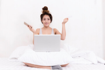 Asian women in sporty pajamas sit or chat online with friends or shopping online. And relax in bed on holiday.