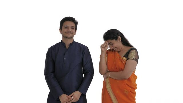 Portrait of young Indian couple. Man pretending hitting the ball with croquet mallet, asking his wife to let him go to the game. Woman expressing annoyance by gestures. Isolated on white background