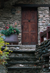 mountain house exterior with stone steps, wooden fence, wooden door with details, vase of pine and pine cones