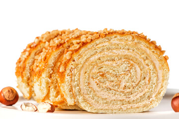 Homemade sweet roll cake with nuts and cream filling in a plate on a white background close-up. Free space for text. Sweet food, homemade cakes. Copy space.