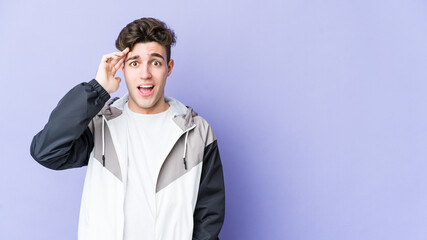 Young caucasian man isolated on purple background shouts loud, keeps eyes opened and hands tense.