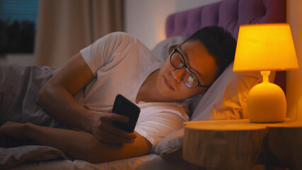 Side view portrait of young asian man using smartphone in bed at night
