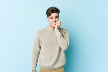 Young caucasian man isolated on blue background biting fingernails, nervous and very anxious.