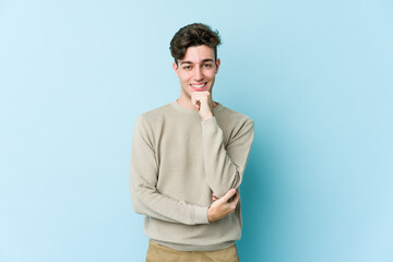 Young caucasian man isolated on blue background smiling happy and confident, touching chin with hand.
