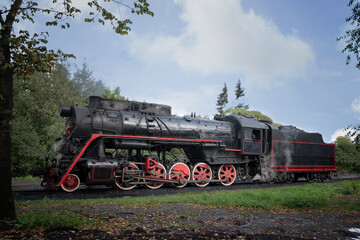 Fototapeta na wymiar Large black steam locomotive with red wheels on rails in the forest