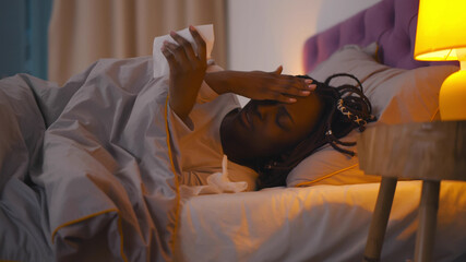 Sick afro woman having headache lying in bed covered with blanket at home