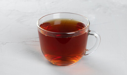 Dark tea in a glass transparent cup with hot water on a concrete background