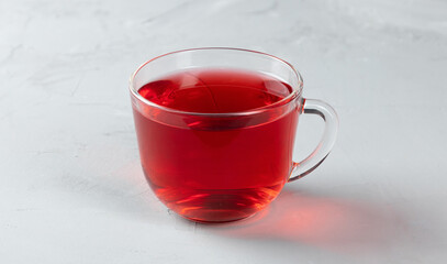 Red tea in a glass transparent cup with hot water on a concrete background