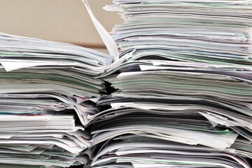 Office paperwork stacked haphazardly on a desk, closeup image. Overworked concept in business environment.