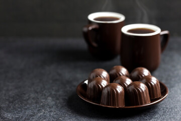 Chocolate candies on a plate and two cups of coffee on black background