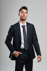 Young man with beard wearing a dark blue suit whit his right hand inside the trousers pocket looking to camera.