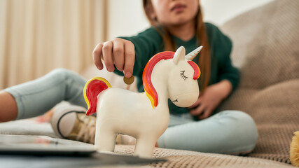 A small girl putting the last coin into her white unicorn moneybox © Svitlana