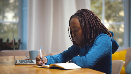 Young african female student sitting at table, using laptop when studying