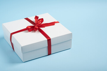 Obraz premium Luxury white gift box with red ribbon on blue background with copy space. Minimalist composition. Universal holidays concept Mother's Day, Valentine's Day, Christmas, New Year, Birthday, discounts.