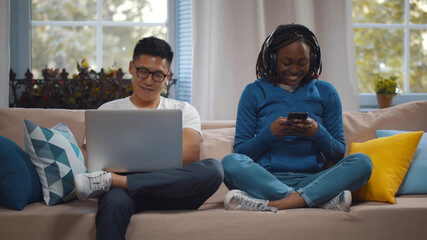 Obraz premium Happy multiracial couple with modern gadgets networking or messaging at home