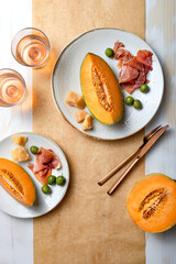 Fresh cantaloupe melon with ham, cheese and green olives with glass of rose wine. Traditional Spanish and Italian appetizer, antipasti snack. Top view