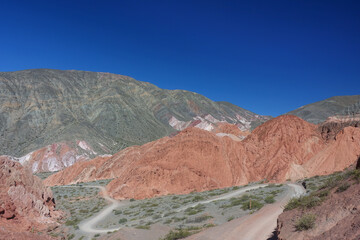 Fototapeta na wymiar A dirt road winds through colorful mountains behind the town of Purmamarca, Humahuaca Valley, northern Argentina
