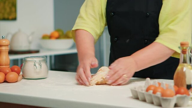 Woman hands kneading dough on table, preparing pastry and kitchen products. Retired elderly baker with bonete mixing ingredients with wheat flour for baking homemade cake and bread