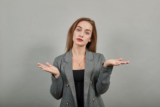 Young attractive woman, dressed gray jacket, with green eyes, light brown hair, background. Palms up, place your product here, raising arms wide spread is catching something.