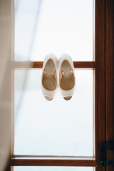 White bride's shoes on a wooden window frame on a white background.