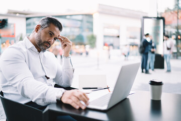 Middle aged businessman watching received video message pondering on strategy information during distance job in sidewalk, thoughtful male employee reading financial publication analyzing trade