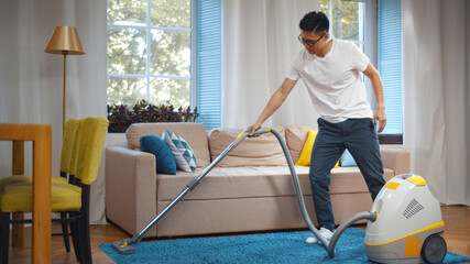 Young asian man cleaning house with vacuum cleaner