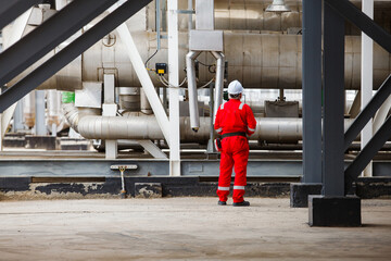 Engineer in white helmet and red work wear on metal pipe and tubes background. Oil refinery and gas...