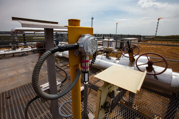 Uralsk region, Kazakhstan - May 24 2012: Oil refinery plant. Pipes, valves and gauge meters. Gas torch on grey sky background. Focus on foreground.