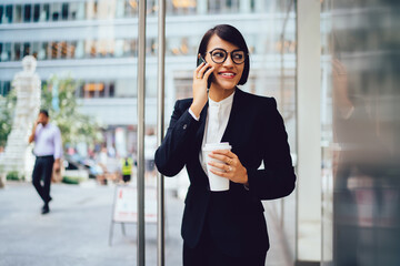 Positive businesswoman talking on smartphone on street