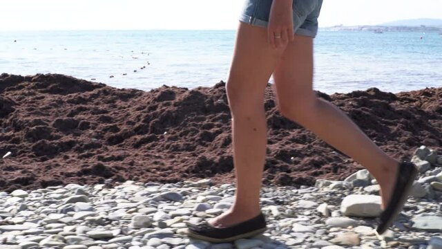 Side view of woman legs walking towards the sea side. Media. Slim and young girl enjoying freedom of beautiful ocean on a sunny sumer day during vacation.