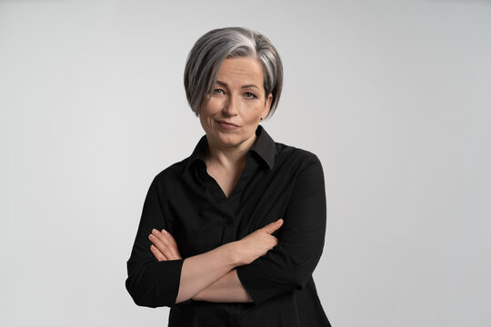 Middle-aged woman with gray hair folded her arms on her chest and smirks at camera. Adult disgruntled woman on an isolated background. High quality photo.