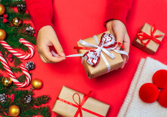 Christmas gifts, children's hands open a new year's gift on a red background, Christmas composition fir branches with gifts, gold-colored decorations, red balls and caramel on a red surface