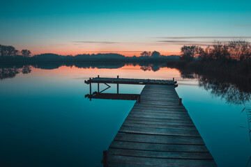 Obraz premium Wooden pier and a view of a calm lake after sunset
