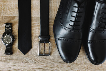 New men's shoes, belt, tie and wristwatch in black on a wooden texture.