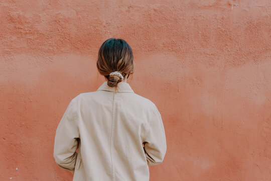 Backless girl with a messy bun with an orange wall on the background