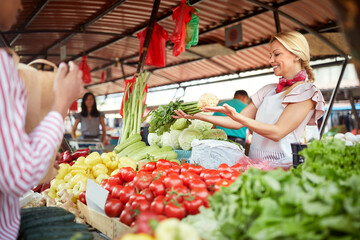Seller woman offers fresh and organic vegetables at the green market or farmers market stall.  Young buyers choose and buy products for healthy food in grocery. All for diet healthy eating, lifestyle.
